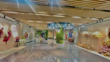 A spacious corridor with a polished floor, decorative floral arrangements, and a modern ceiling design.