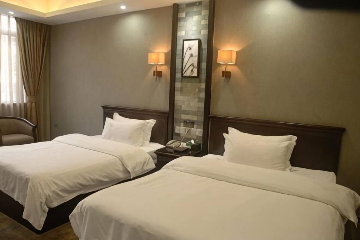 Quarto de hotel com duas camas, uma mesa de cabeceira, um abajur e uma janela com cortinas.