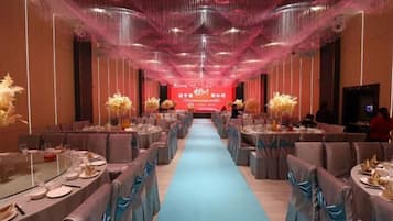 A banquet hall with tables set for a formal event, a stage with a red backdrop, and a blue carpet leading to the stage.