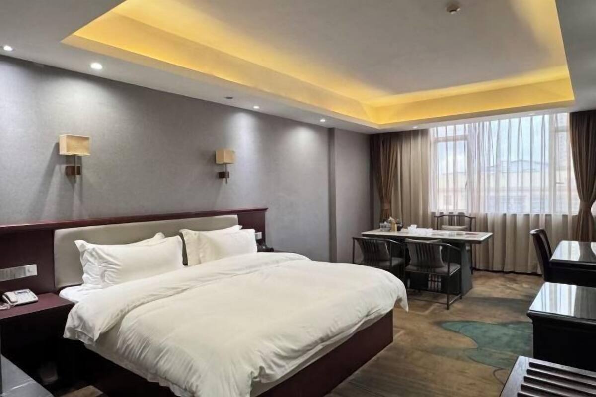 Quarto de hotel com cama, mesa de cabeceira, escrivaninha, cadeiras e vista para o exterior.