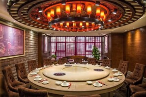 Une salle de conférence avec une table ronde, des chaises marron et un grand lustre.