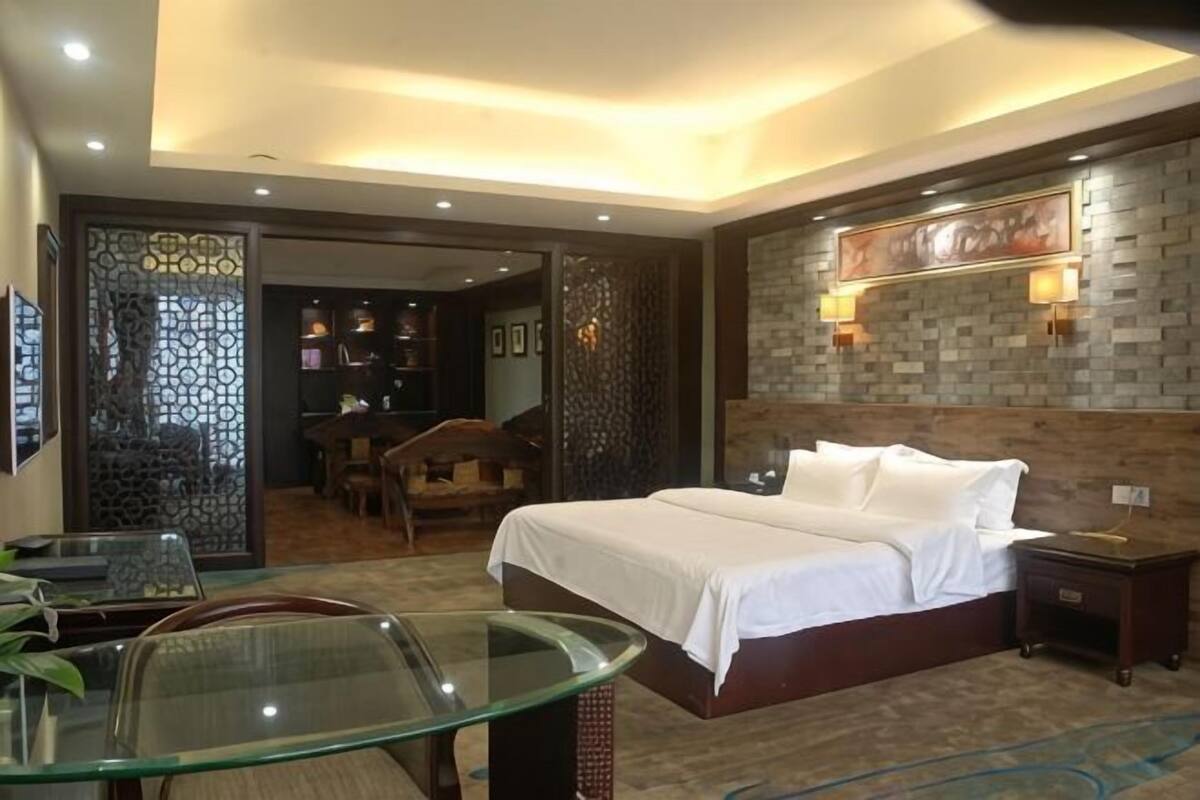 Quarto de hotel com cama, mesa de vidro, cadeira, mesa de cabeceira e decoração na parede.