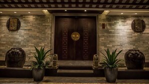 A hotel entrance with a dark wooden door, stone wall, and potted plants. - Hengsheng Kejia Courtyard (Xinfeng)