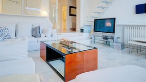 A modern living room with a glass coffee table, white sofas, a flat-screen TV, and a staircase. - Villa Bonanova Style (Palma)
