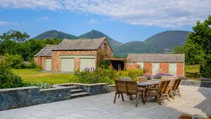 Un patio con una mesa y sillas, un muro de piedra y vistas de un edificio de ladrillo con un garaje.