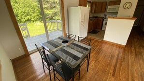 Een eetgedeelte met een tafel en stoelen, een koelkast, en een keuken met houten kasten en apparatuur.