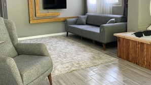 A modern living room with a grey sofa, a green armchair, a wooden TV stand, and a herringbone-patterned floor. - Karadeniz Suit (Ardeşen)