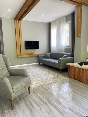 A modern living room with a grey sofa, a green armchair, a wooden TV stand, and a herringbone-patterned floor. - Karadeniz Suit (Ardeşen)