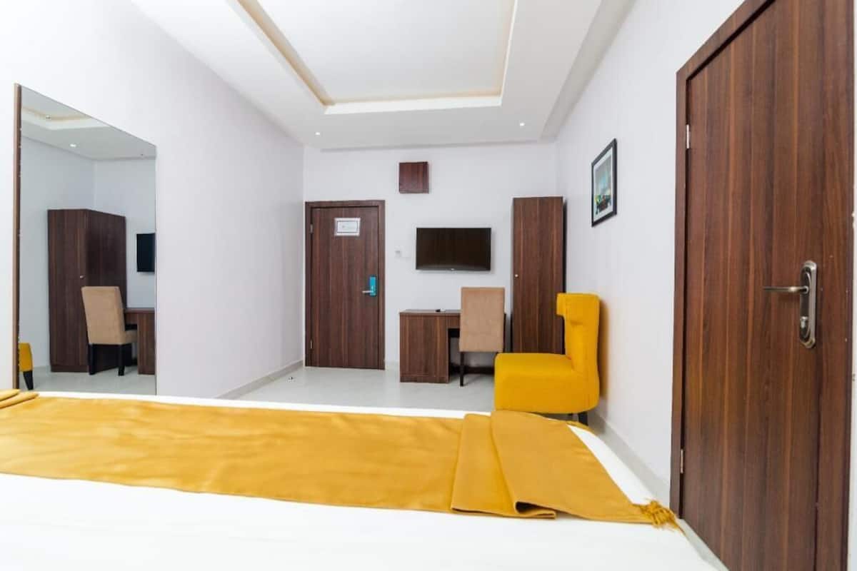 A hotel room with a bed, a desk, a chair, a television, and a wardrobe.
