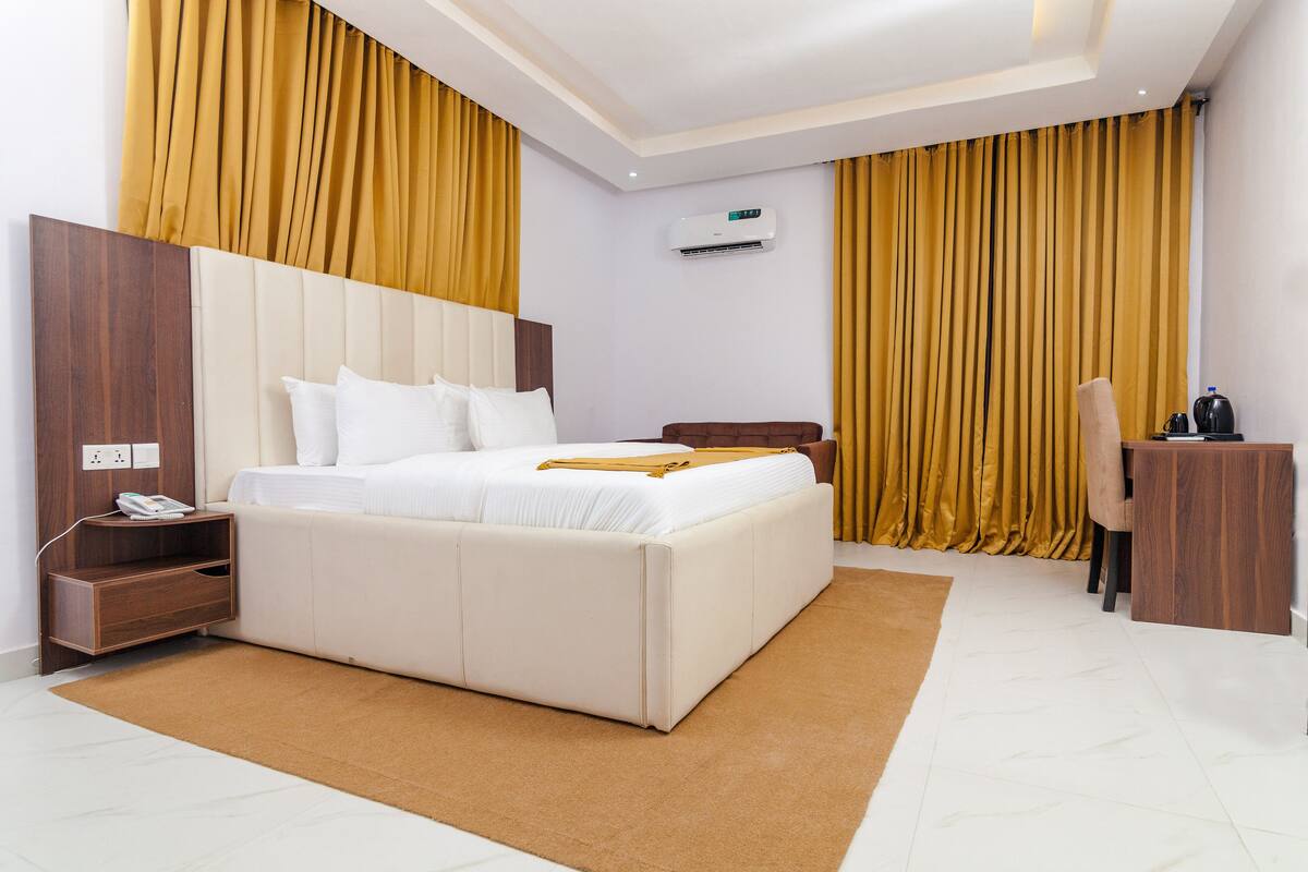 A modern hotel room with a large bed, a wooden nightstand, a desk, and a chair.