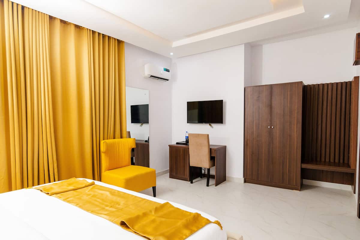 A hotel room with a bed, a desk, a chair, a wardrobe, and a television.