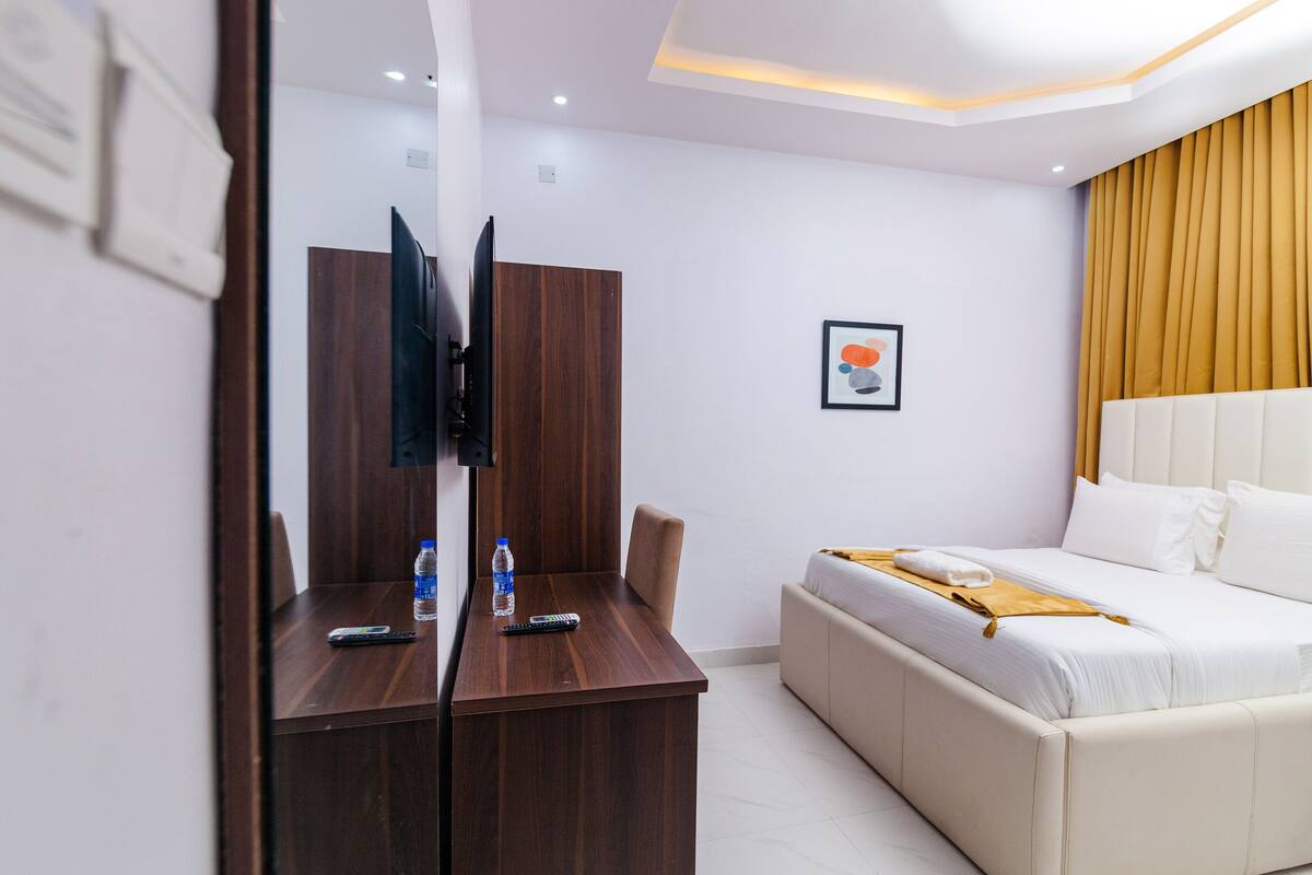 A hotel room with a wooden desk, a bed with white bedding, a television mounted on the wall, and a framed picture on the wall.