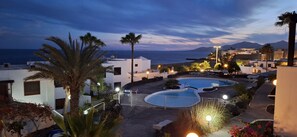 Un complexe hôtelier doté d’une piscine, de palmiers et offrant une vue sur la mer au crépuscule.