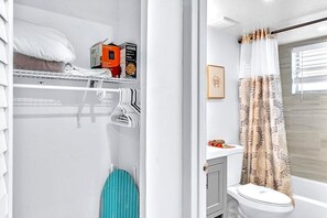 A compact bathroom with a toilet, shower curtain, and a small shelf with toiletries. - Hollywood Large Studio Close to Beach & Casino LB3 (Hollywood)
