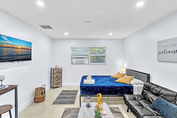 A modern hotel room with a bed, a sofa, a desk, and a window with blinds. - Hollywood Large Studio Close to Beach & Casino LB3 (Hollywood)