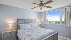 Una camera da letto con un letto, comodini, una ventola a soffitto e una finestra vista oceano.