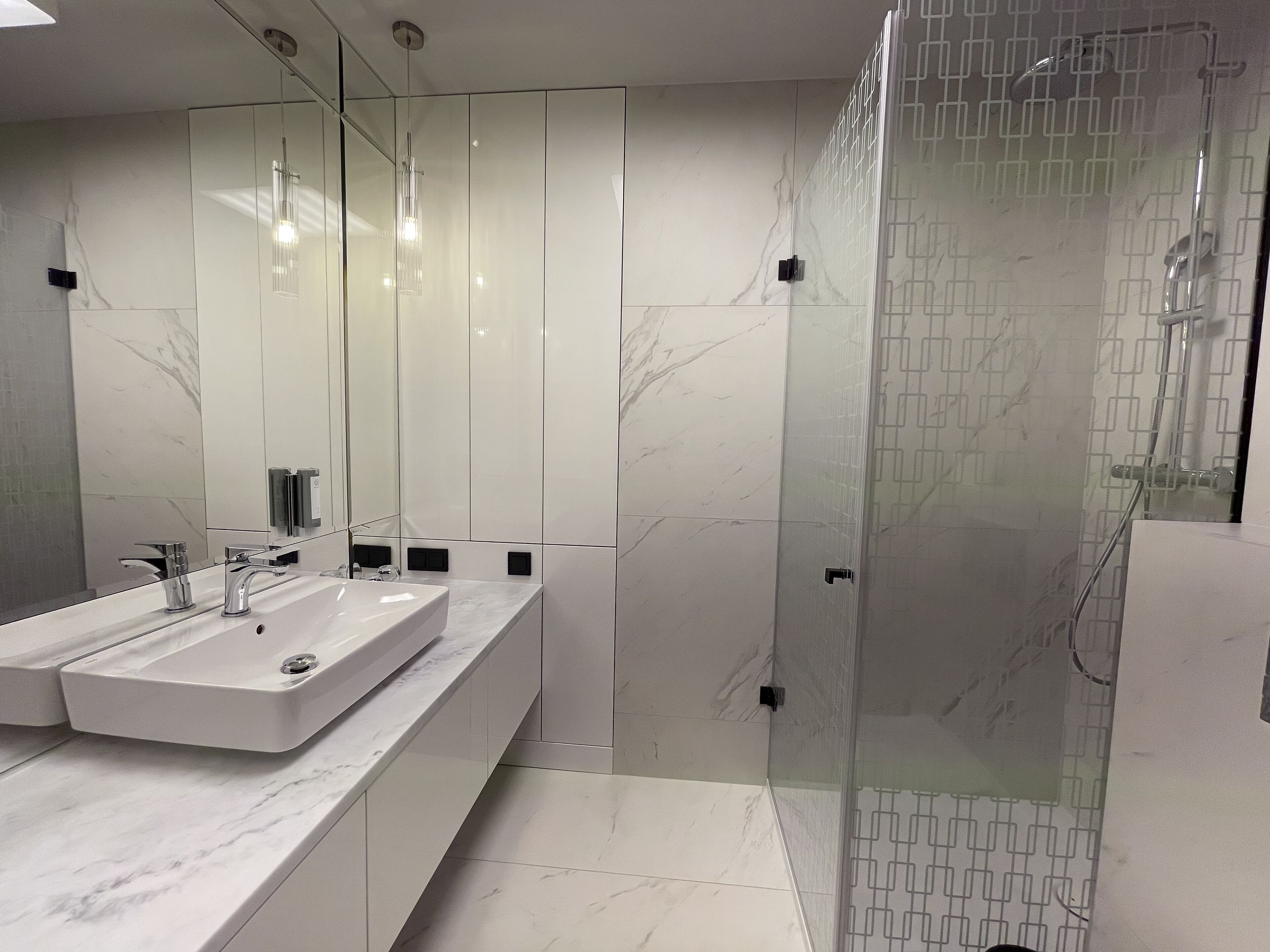 Un bagno moderno con uno specchio grande, due lavandini e una cabina doccia in vetro.