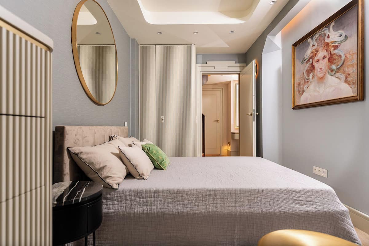 Ein Schlafzimmer mit einem Bett, einem runden Spiegel, einem Bild und einer Tür zu einem anderen Raum.