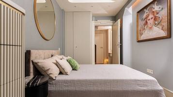 A bedroom with a bed, a round mirror, a painting, and a door leading to another room.