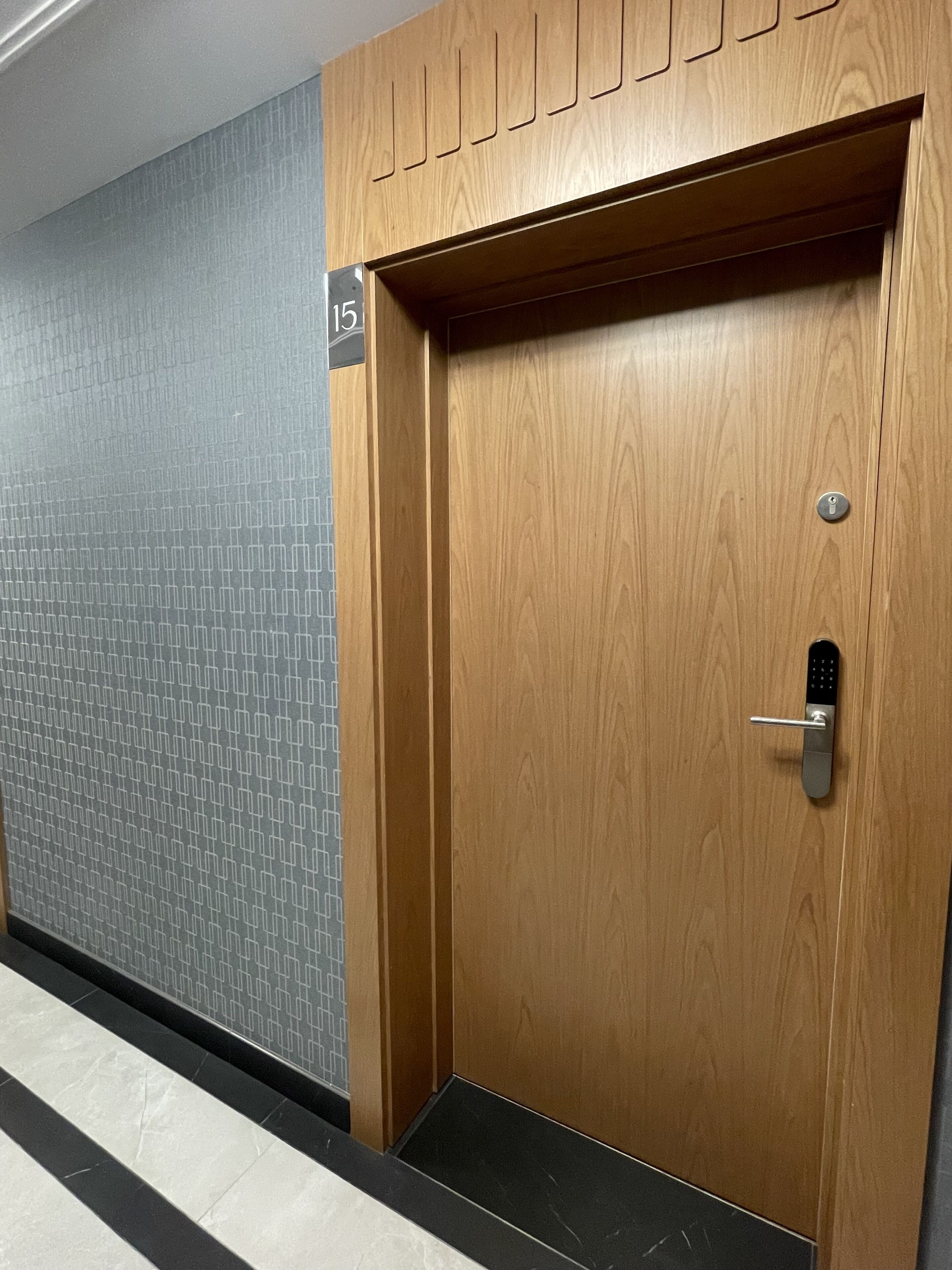 A wooden door with a keyhole and a numeric keypad lock, adjacent to a wall with a geometric pattern and a number sign.