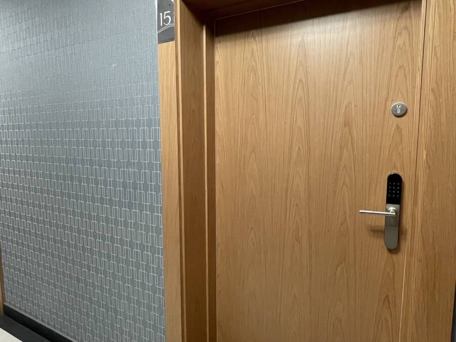 A wooden door with a keyhole and a numeric keypad lock, adjacent to a wall with a geometric pattern and a number sign.