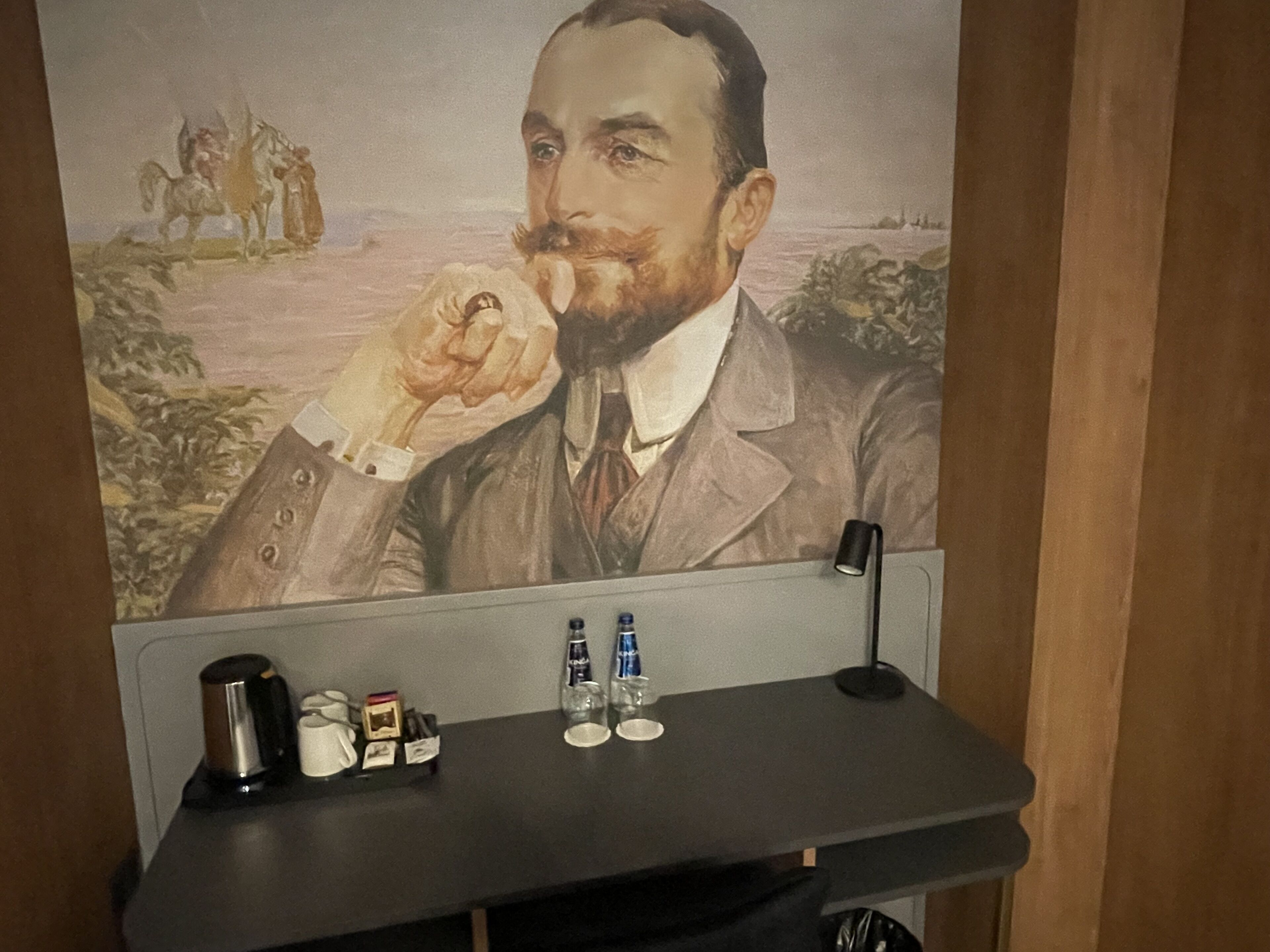 Un mur orné d’un portrait et un bureau avec une machine à café, des bouteilles et des verres.