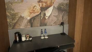 Un mur orné d’un portrait et un bureau avec une machine à café, des bouteilles et des verres.