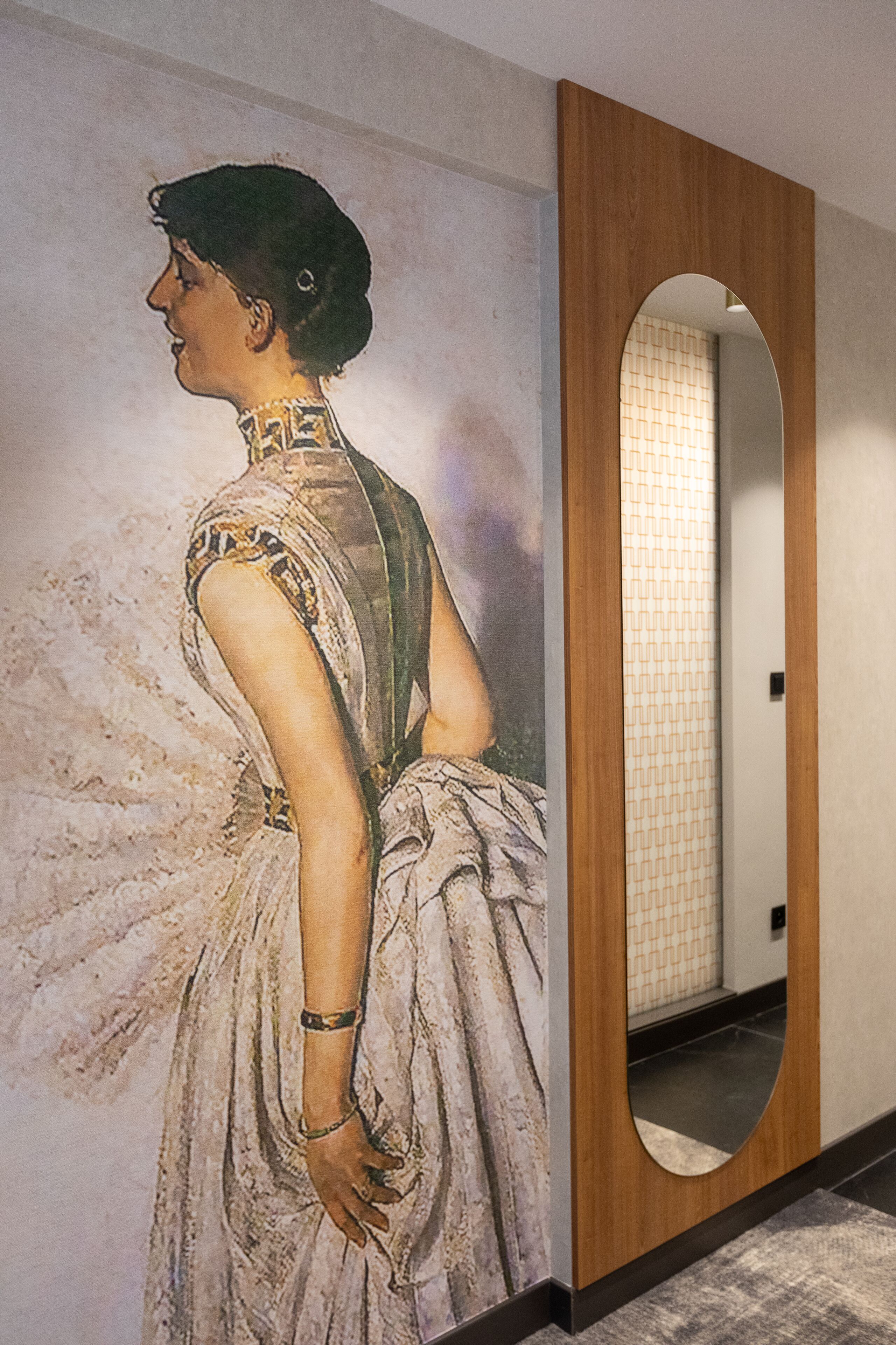 Ein Korridor mit einer großen Wandmalerei, die eine Frau in einem Kleid zeigt, einem hölzernen Türrahmen und einer gefliesten Wand.