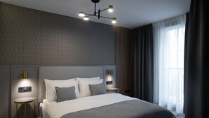 Een moderne hotelkamer met een groot bed, twee nachtkastjes, een wandlamp en een groot raam met gordijnen.