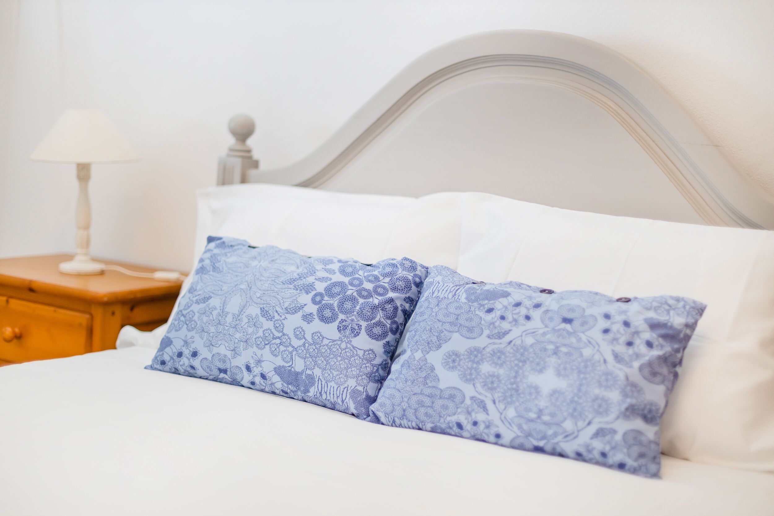 Una cama con ropa de cama blanca y dos almohadas con estampado azul.