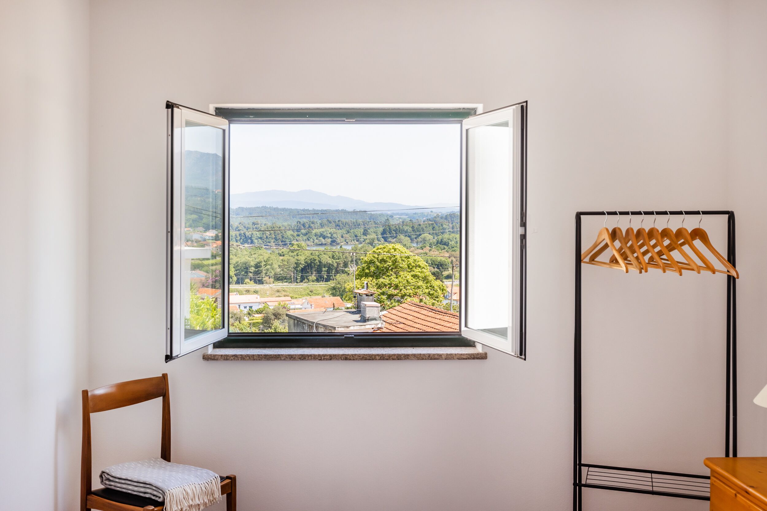 A room with a large window offering a view of a mountainous landscape and a hanging wooden clothes rack.