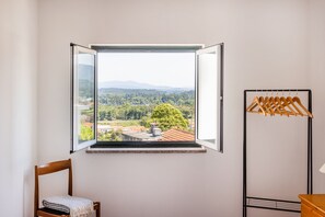 Habitación con un amplio ventanal que ofrece vistas a un paisaje montañoso y un perchero de madera colgante.