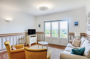 A living room with a sofa, armchairs, a TV, and a small table. There is a balcony with a view of greenery. - Casa da Leira (Vila Nova de Cerveira)