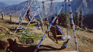A swing set with a metal frame and chains, situated on a grassy area with mountains in the background. - Camp Awara Dhanaulti (Dhanaulti)