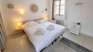 A neatly arranged bedroom with a large bed, bedside lamps, a window with curtains, a radiator, and a small bedside table. - HENRI CAMILLE REAL ESTATE - Florida 2 - 2 bedrooms close center (Cannes)