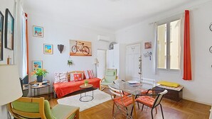 A living room with a sofa, chairs, a glass table, and a bicycle painting on the wall. - HENRI CAMILLE REAL ESTATE - Florida 2 - 2 bedrooms close center (Cannes)
