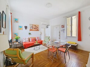 A living room with a sofa, chairs, a glass table, and a bicycle painting on the wall.