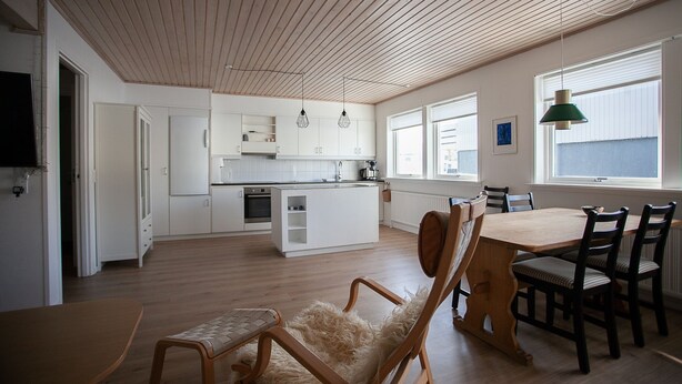 A modern kitchen with white cabinets and a wooden island, a dining area with a wooden table and chairs, and a large window providing natural light. - 3BR - Townhouse - Free Parking -Tórshavn (Hoyvík)