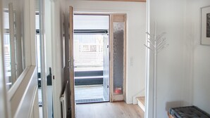 A hallway with wooden flooring, a black rug, a white coat stand, and a bench with a cushion. - 3BR - Townhouse - Free Parking -Tórshavn (Hoyvík)