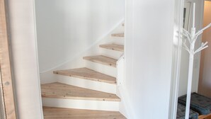 A spiral staircase with wooden steps and white walls, leading to a landing area with a white floor lamp and a bench. - 3BR - Townhouse - Free Parking -Tórshavn (Hoyvík)