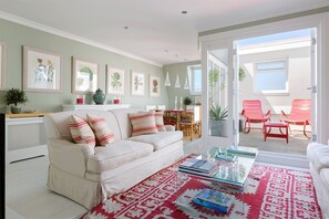 A living room with a sofa, coffee table, and red patterned rug. There is a dining area with a table and chairs, and a balcony with red chairs. - Lovely two bedroom flat with patio in Notting Hill (London)