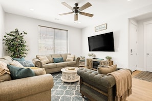 A living room with a beige sofa, a grey armchair, a coffee table, a television, and a ceiling fan.