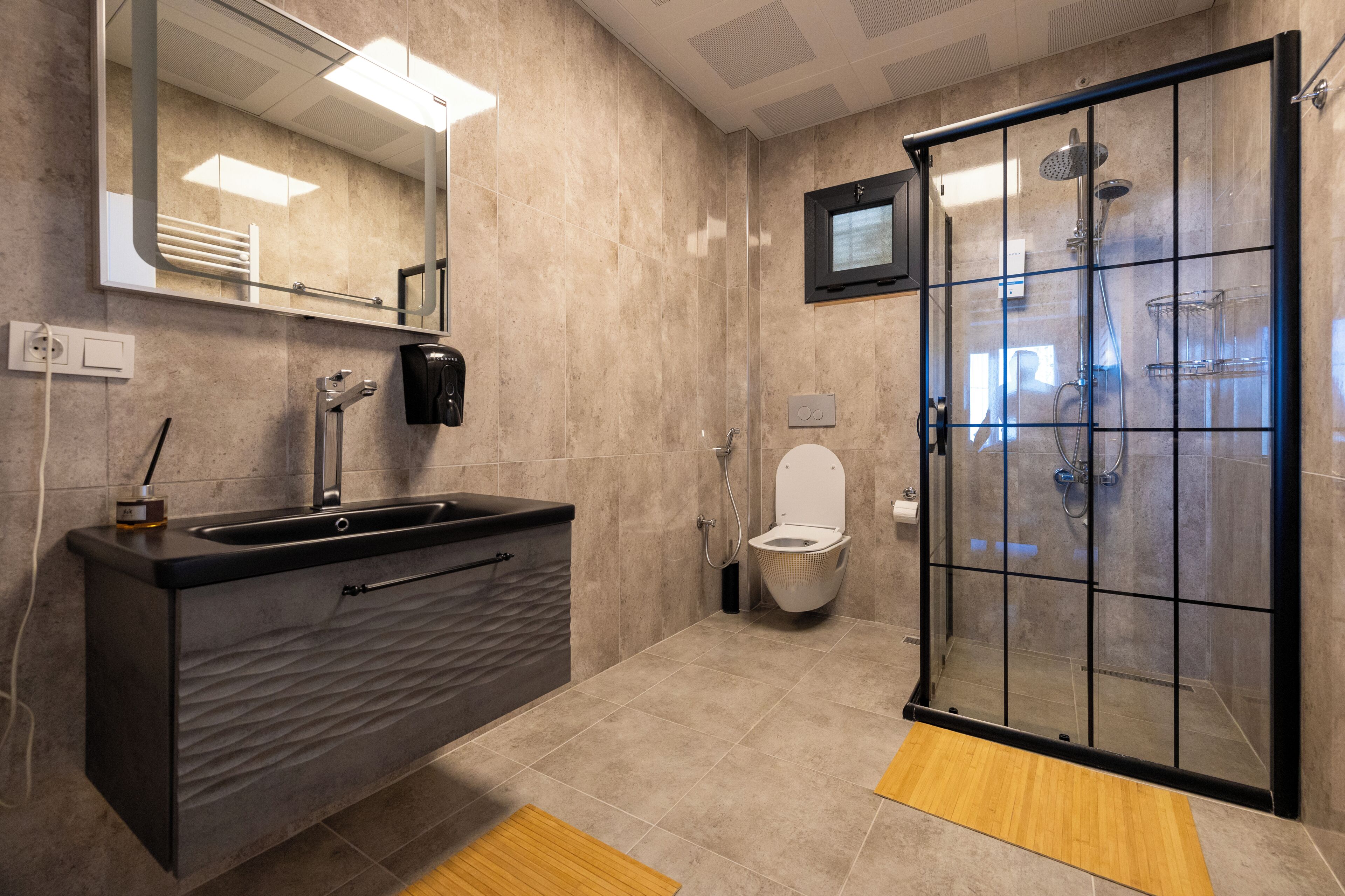 Un baño moderno con ducha envuelta en vidrio, un tocador negro con lavabo y un inodoro.