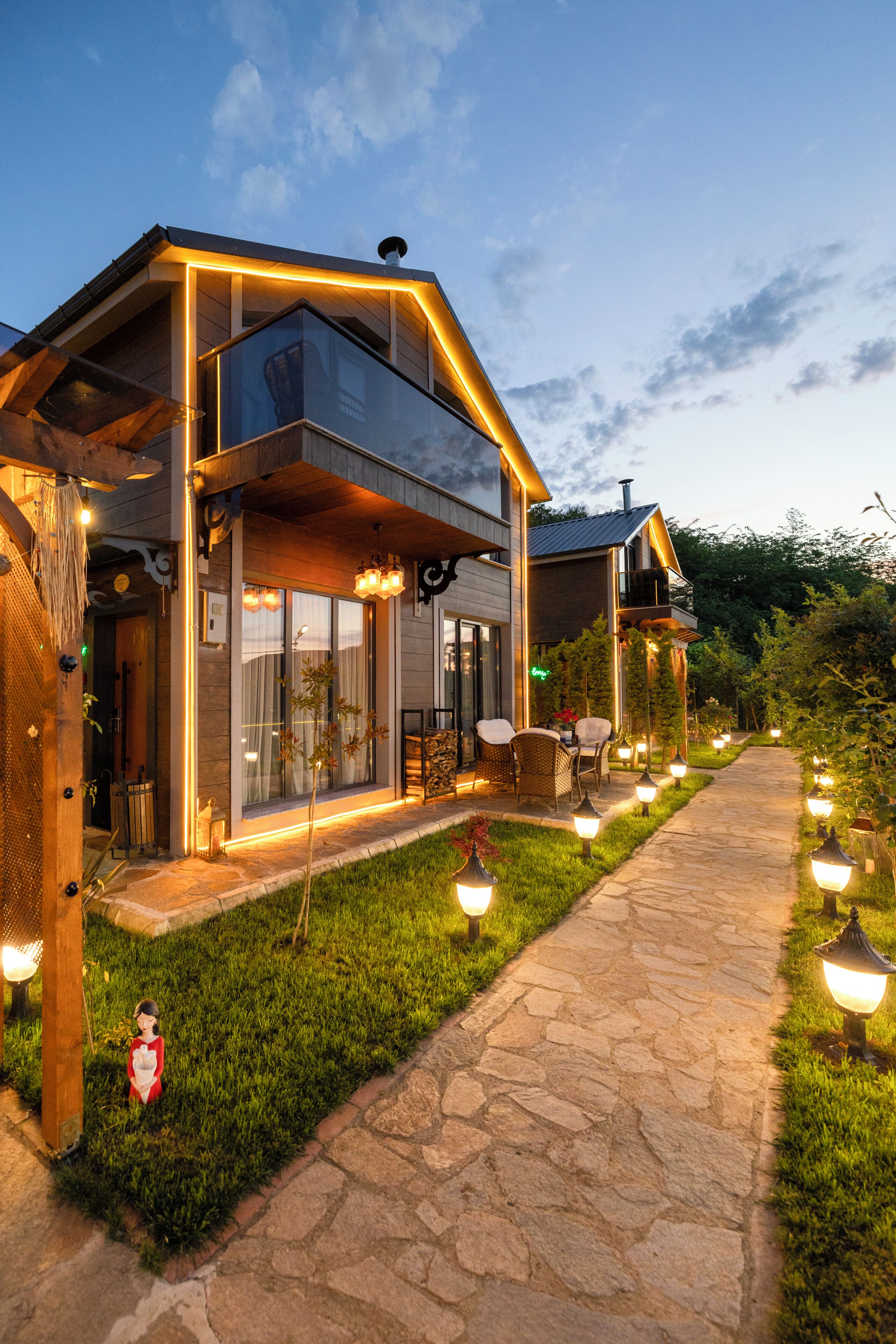 A modern house with a stone pathway, outdoor seating, and string lights.