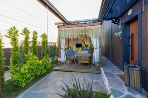 A wooden deck with a thatched roof, a table with chairs, and a small TV. - Poison Garden Suite & SPA (Trabzon)