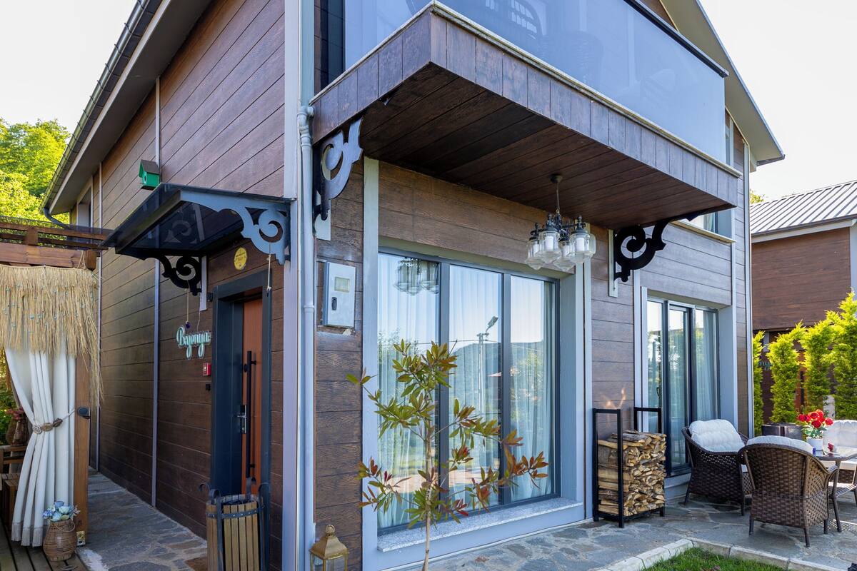 A modern two-story house with a covered patio, large windows, and a stone pathway leading to the entrance.