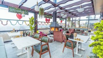 An outdoor restaurant with tables and chairs, a fireplace, and hanging plants.