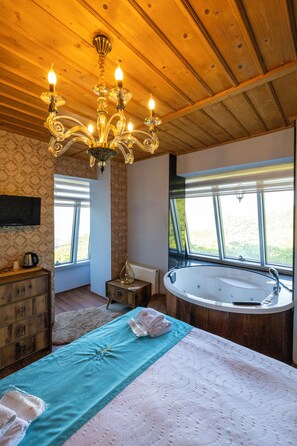 A bedroom with a wooden ceiling, a chandelier, a large window, a bathtub, and a bed with a blue and white bedspread. - Poison Garden Suite & SPA (Trabzon)