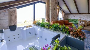 Een wellnessruimte met een jacuzzi, een groene gestoffeerde bank en een raam met planten.