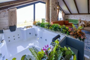 Un área de spa con un hidromasaje, un sofá verde acolchado y una ventana bordeada de plantas.